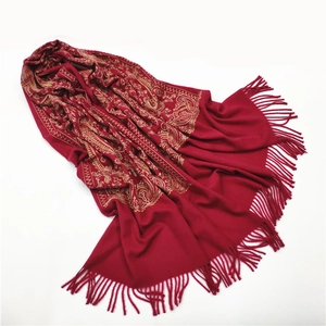 Detailed view of red cashmere shawl with golden paisley embroidery and fringe trim