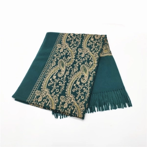 Close-up of golden paisley embroidery and tassel detail on dark green winter shawl
