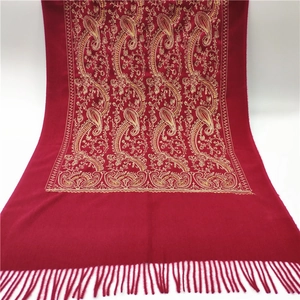 Detail view of golden paisley embroidery and tassel fringe on a red cashmere scarf