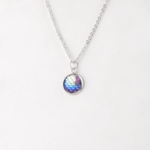 Macro detail of round mermaid scale pendant with blue and purple gradient on silver chain