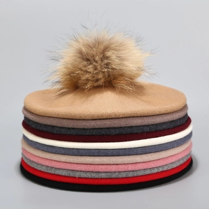 Stacked wool knit berets in multiple colors with fluffy faux fur pom poms on top