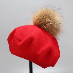 Detail of red knitted wool beret showing plush fur pompom and fine textured knit pattern
