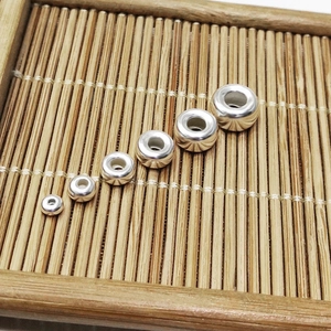 Size comparison of silver metal spacer beads on a bamboo mat for DIY jewelry making