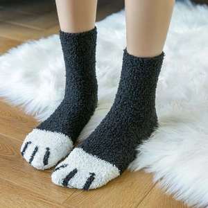 Close-up of plush coral fleece cat paw socks on a white rug and wooden floor