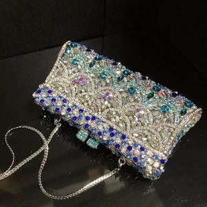 Angled view of a silver and blue rhinestone clutch bag with a delicate chain strap