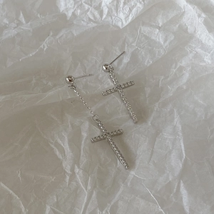 Detailed view of asymmetric silver cross earrings with shimmering white zircon stones