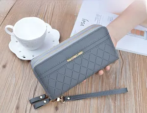 Detail of grey quilted double zipper wallet held by hand with wrist strap and metal logo