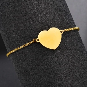 Polished gold heart charm bracelet with adjustable box chain displayed on a dark stand