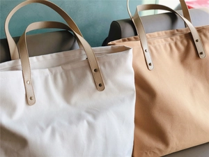 Detail view of large canvas tote bags with leather handles and metal rivet reinforcement