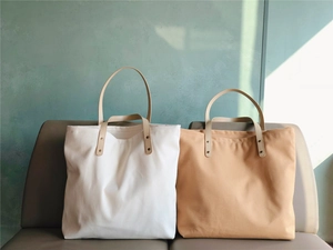 Detail of canvas tote bags with leather handles on a leather bench in natural sunlight