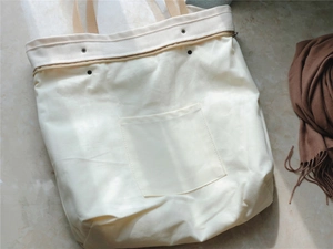Detailed view of cream canvas tote bag with brown leather handles and square front pocket