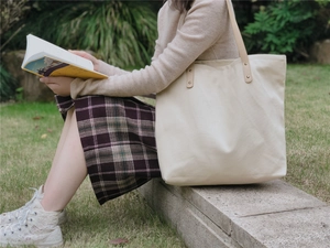 Detail of beige canvas tote bag with leather handles in a serene outdoor setting