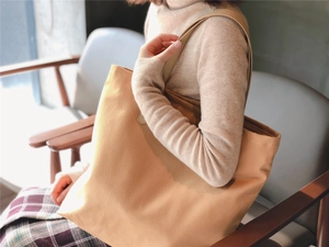 Brown canvas tote bag with leather straps shown on shoulder for daily commute style