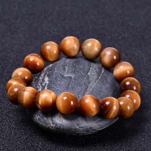Detailed view of natural tiger eye stone beads on dark rock with golden chatoyant effect