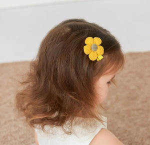 Detail of a child wearing a yellow corduroy flower hair clip on brown curly hair