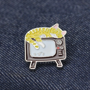 Détail d'un pin's émaillé vintage avec chat tigré sur un vieux téléviseur et texte japonais