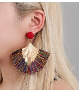 Close-up of fan-shaped bohemian tassel earrings with red studs and golden metal details