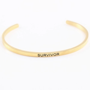 Détail du bracelet mantra en acier doré avec gravure Survivor sur la surface