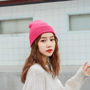 Close-up of a bright rose red knitted beanie hat worn by a model in outdoor lighting