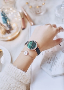 Close-up of a women's watch with a green marble dial and a matching gold letter M bracelet