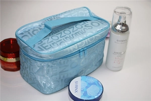 Detail view of a light blue makeup bag with white letter patterns and top handle
