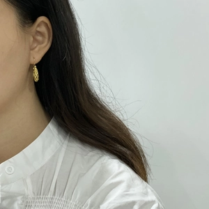 Macro detail of gold ethnic hollow earrings on a model wearing a white shirt