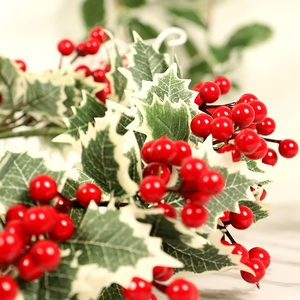 Gros plan de baies rouges artificielles et feuilles de houx à bords blancs de Noël