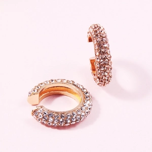 Detail of C-shaped gold clip-on earrings with pavé white rhinestones on pink background
