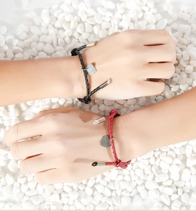 Close-up of black and red braided PU cord bracelets with heart pendants on white pebbles