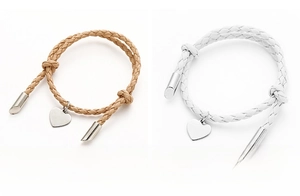 Detail view of woven couple bracelets in khaki and white with metal heart charms