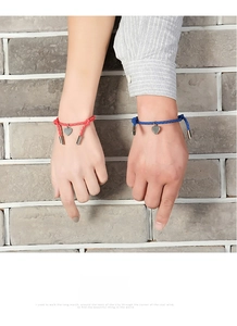 Matching hand-woven couple bracelets in red and blue with silver heart pendants on wrist
