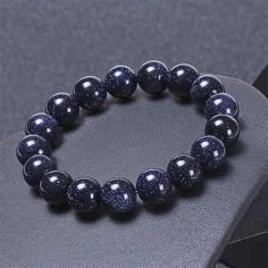 Macro shot of 10-12mm blue sandstone beads showing starry glitter on a grey stand
