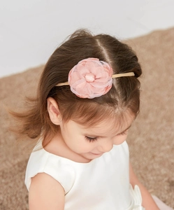 Close-up of a baby girl wearing a pink fabric flower headband with pearl detail