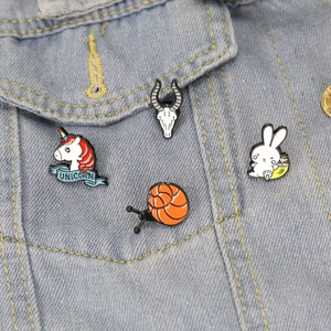 Detail of colorful snail and animal enamel pins on a light blue denim jacket pocket