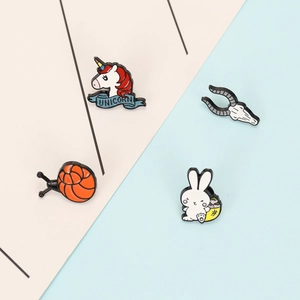 Detail of four colorful enamel lapel pins featuring unicorn, snail, rabbit and skull designs