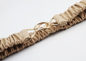 Close-up of elastic beige waist belt with pleated leather texture and gold metal buckle
