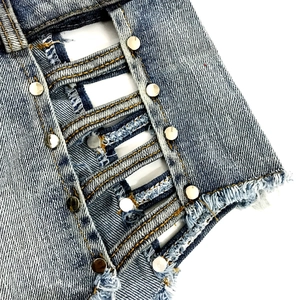 Dettaglio del tessuto denim blu con borchie in metallo argentato e bordi sfrangiati sugli shorts