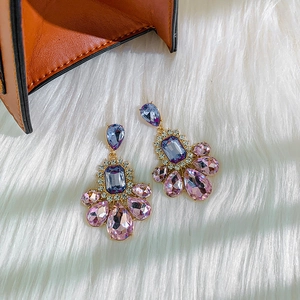 Close-up of long drop earrings with purple crystals and sparkling rhinestones on white fur