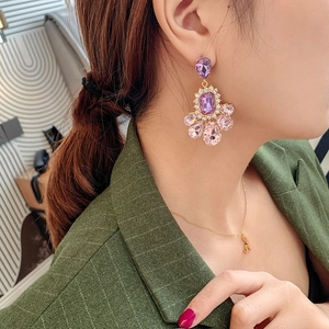 Close-up of model wearing gold drop earrings with purple and pink teardrop crystals
