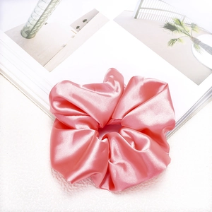 Detailed view of pink satin scrunchie placed on white faux fur and magazine background