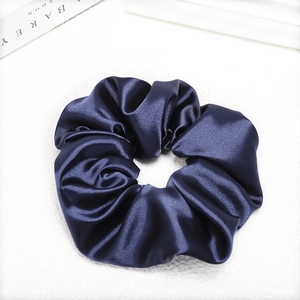 Detailed view of dark blue satin scrunchie with smooth texture on marble background