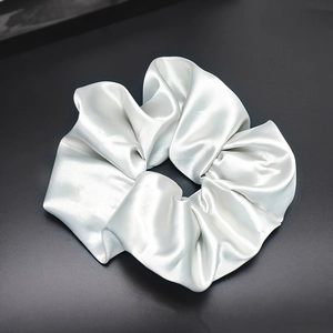 Detailed close-up of shiny silver satin scrunchie with smooth silk-like texture