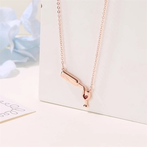 Detail of rose gold wine bottle necklace with heart-shaped red gem on white stand