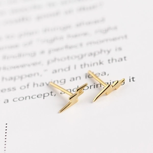 Macro shot of gold lightning bolt stud earrings on a vintage paper background