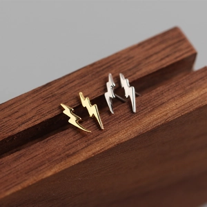 Macro shot of minimalist gold and silver lightning bolt stud earrings on wood