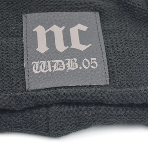 Detail of black knit beanie with gray leather patch featuring gothic lettering and texture