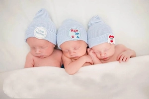 Three newborns sleeping in striped knit hats with Little Brother embroidery detail