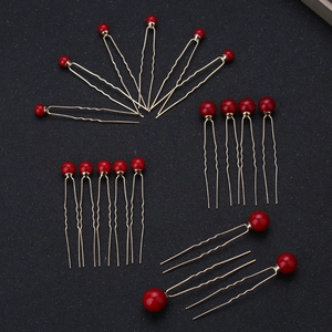 Detail of 20 gold U-shaped hair pins with red pearl accents for bridal hairstyling