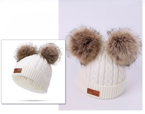 Detail of cable knit toddler beanie with faux fur double pom-poms and leather logo patch
