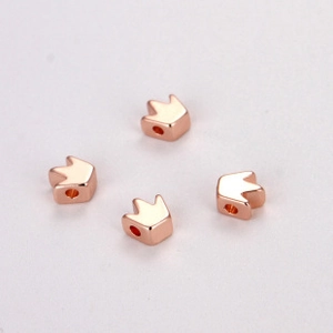 Close-up of four rose gold crown-shaped beads for DIY jewelry making on white background
